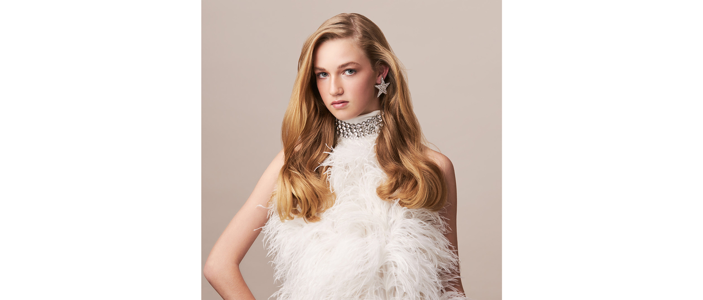 Model with golden waves in a high-fashion feathered outfit.